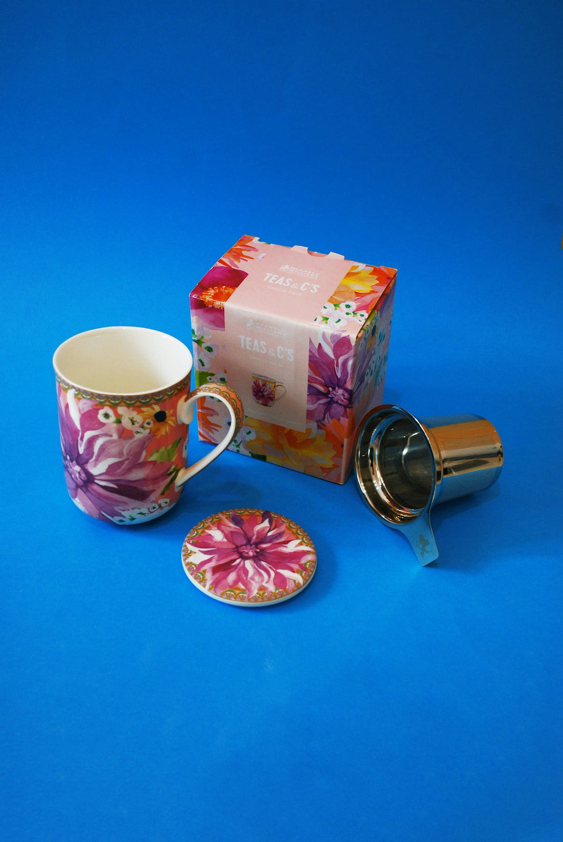 Floral mug, coaster, tea strainer, and box on blue