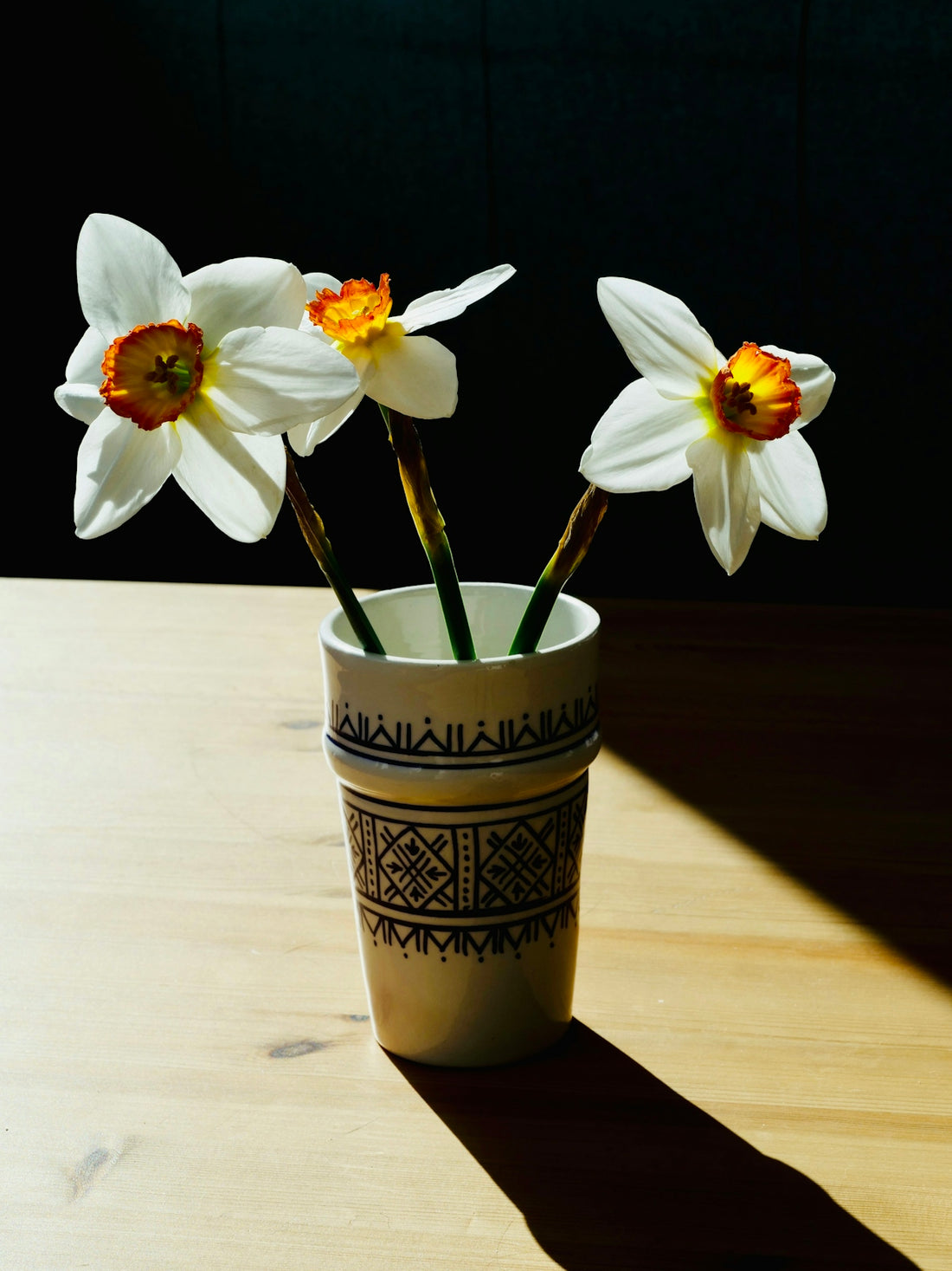 Three white daffodils in a decorative vase on a table.