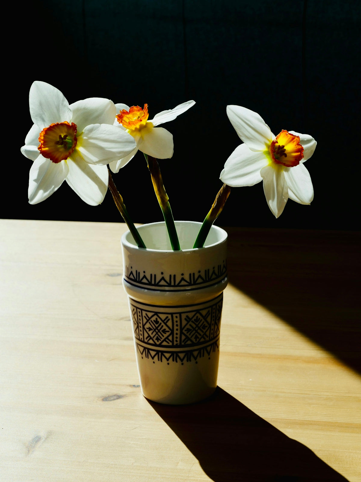 Three white daffodils in a decorative vase on a table.